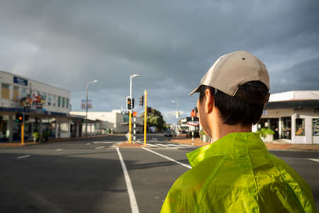 Man stopping at the intersection with orange traffic light. Out-of-focus streets and shops in the background, at Milford, Auckland.の写真素材