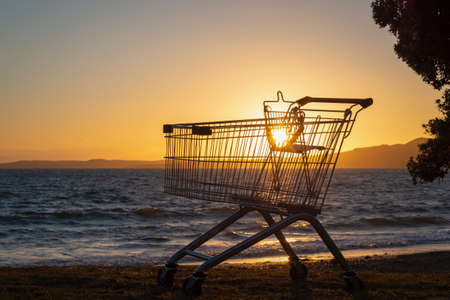 Backlit supermarket trolley abandoned on Milford beach, Rangitoto Island in the distance. Auckland.の写真素材