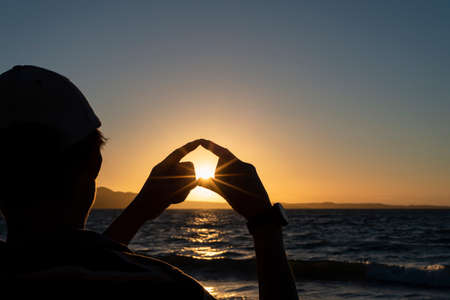 Silhouette of a man with hands forming a heart shape at sunrise.の写真素材