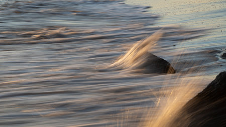 Ocean waves crashing on the rocks of sandy beach at sunrise
