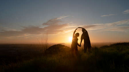 Silhouette of a couple standing on hilltop with raising arms embracing the sun. One Tree Hill, Auckland.の写真素材