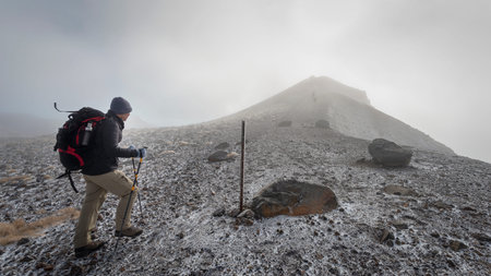 Hiking the steep scree terrain to the Red Crater summit with strong southerly wind on Tongariro Alpine Crossing. New Zealand.の写真素材