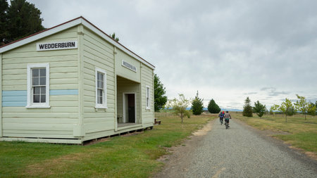 Three cyclists riding the Otago Central Rail Trail, passing Wedderburn station. South Island.のeditorial素材