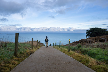 Man walking on Tunnel Beach track. Stormy clouds gathering at the horizon. Dunedin.