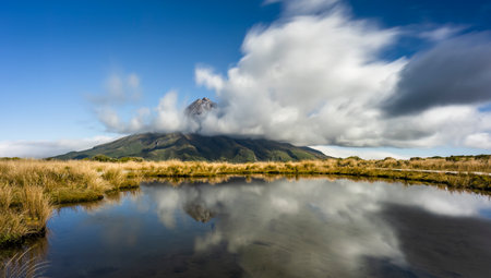 Mt Taranaki reflected in the Pouakai tarn. Clouds floating around the mountain peak. Taranaki. New Zealand.の写真素材