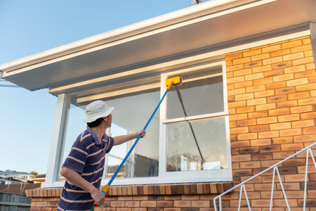 Man washing windows with long pole and brush. Home maintenance project.の写真素材
