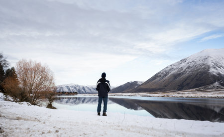Tourist looking at views of Lake Camp in winter. Snow-capped mountains reflected in the clear water. Ashburton Lakes region. Canterbury.の写真素材