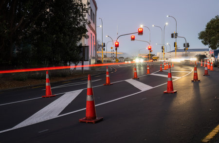 Orange traffic cones lined up on the road. Car light trails on the road intersection. Auckland.の写真素材