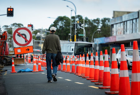 Man walking on the road with orange traffic cones diverting the traffic. Bus and cars on the road under maintenance. Auckland.の写真素材