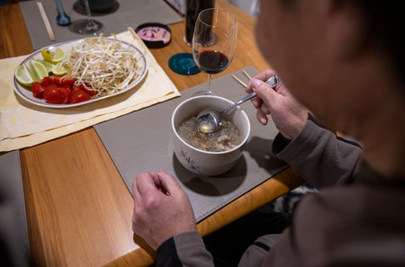 Man eating homemade Vietnamese soup dish Pho at home. Fresh vegetables and red wine glass on the table.の写真素材