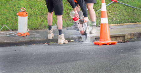Workers cutting concrete footpath above the drainage hole. Hands holding concrete cutting machine. Repairing work on Auckland road.の写真素材
