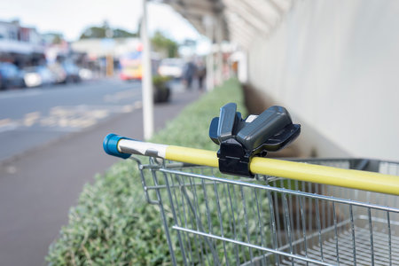 Supermarket trolley with smartphone holder on the handle bar dumped outside shopping mall. Out-of-focus bus and pedestrians on the road. Auckland.の写真素材