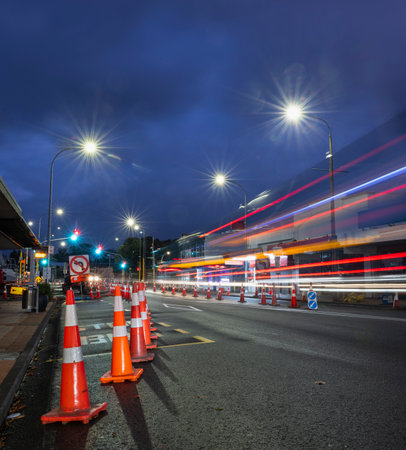 Orange traffic cones lining up the road. Bus light trails approaching the intersection. Roadworks in Auckland. Vertical format.の写真素材
