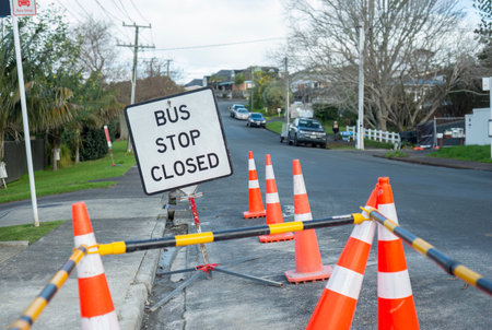 BUS STOP CLOSED sign among orange traffic cones at the bus stop. Unrecognizable cars and people on the street. Repairing flood damaged roads in Auckland.の写真素材
