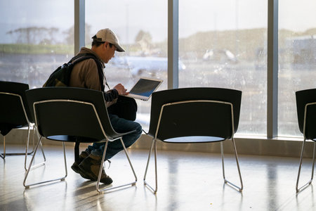 Man working on a laptop computer at the airport. Traveller remote work online in the boarding lounge of Airline hub.の写真素材
