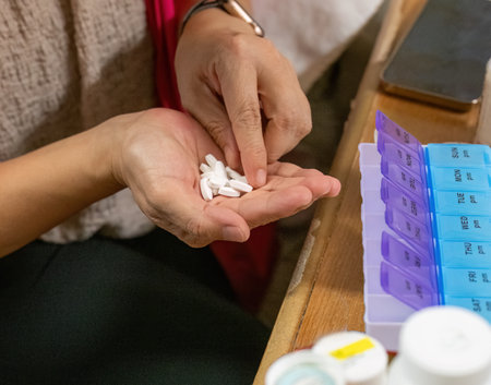 Female hands sorting pills into medical pill boxes. Pill box with the words Mon to Sun, am and pm, for easing daily doses of pills. Smartphone and bottles of medicine on the table.の写真素材