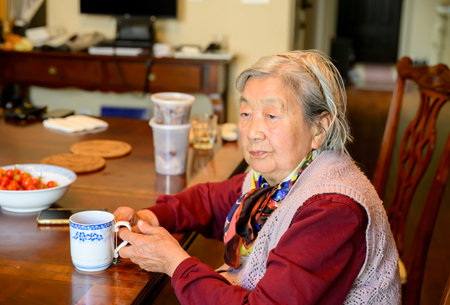 Senior woman with a cup of tea in her hands, sitting by the table at home.の写真素材