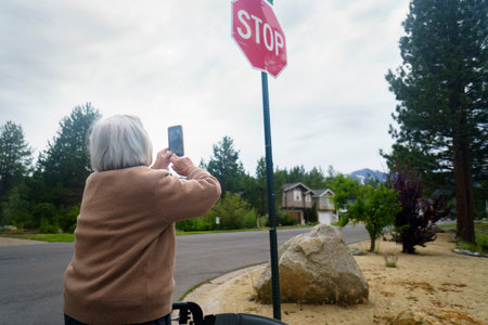 Senior woman taking photos using smartphone by the STOP road sign.の写真素材