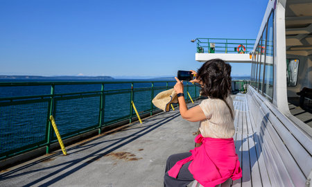 Woman taking smartphone photos of the scenery on the deck of a ferry. Seattle. Washington State.の写真素材