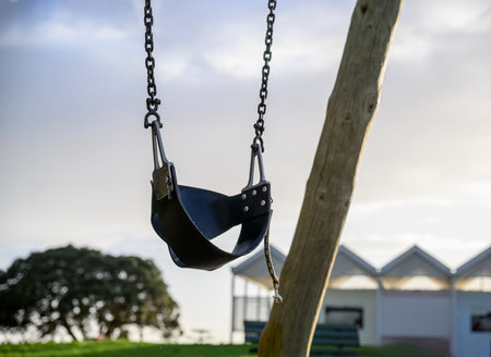 Empty child swing set on an outdoor playground. Low angle view. Milford beach. Auckland.の写真素材