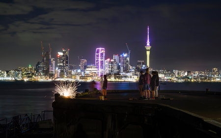 Sky Tower lit up in pink and yellow to celebrate Diwali. Family and friends lighting fireworks for Guy Fawkes. Auckland.のeditorial素材