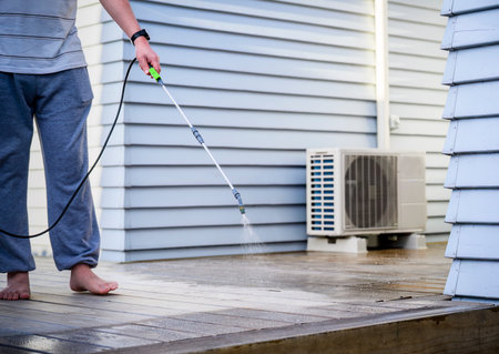 Man cleaning wooden deck with hand-held pressure sprayer, preparing deck before staining.の写真素材