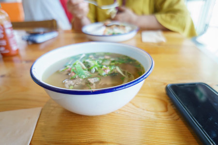 Vietnamese Pho dish on the table. Unrecognizable people enjoying lunch in a restaurant.