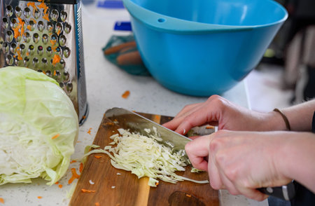 Hands of a woman chopping cabbage for coleslaw in the home kitchen. Left-handed woman holding kitchen knife.の写真素材