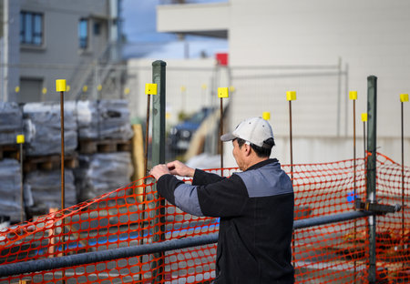 A worker installing the orange safety barrier mesh at a construction siteの写真素材