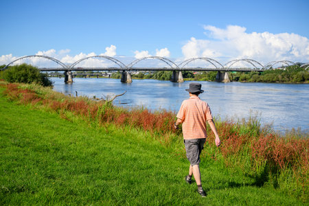 Man walking along Waikato river, Tainui Bridge in the background. Huntly. New Zealand.の写真素材