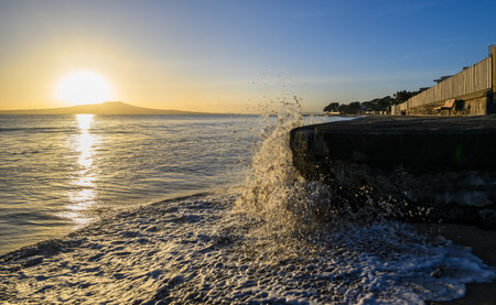 Waves crashing into the concrete seawall. Sunrise over Rangitoto Island. Milford Beach. Auckland.の写真素材