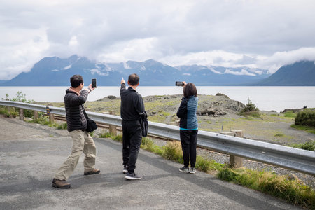 Tourists having fun and taking photos of mountains using smartphones. Seward waterfront. Alaska.の写真素材