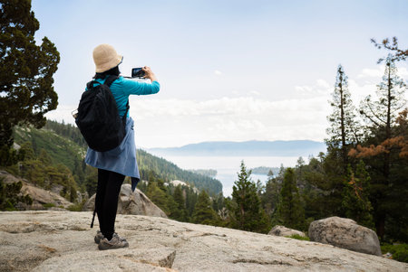 Woman taking photos of Emerald Bay using smartphone. Eagle Lake trail. South Lake Tahoe. California.の写真素材