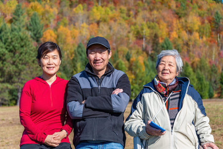 Senior woman and family posing for photos in a park with autumn colours in the background. Mont...