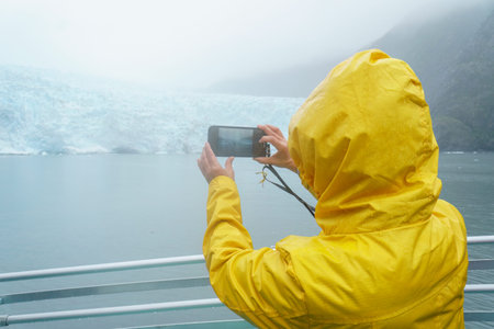 Tourist taking smartphone photos of Holgate Glacier in the rain. Kenai Fjords National Park, Seward,...