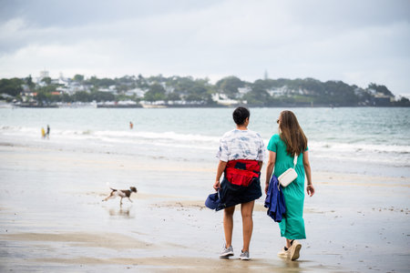 Women walking the dog on the beach. Unrecognizable people playing in the water. Takapuna Beach. Auckland.の写真素材