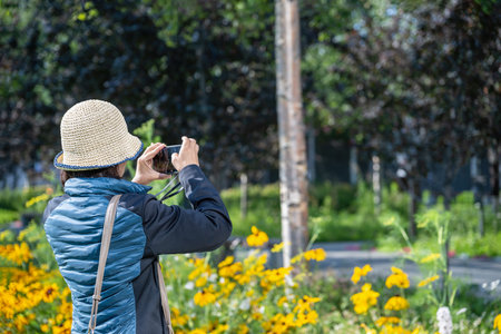 Tourist taking photos of beautiful yellow flowers using a smartphone. Anchorage. Alaska.の写真素材