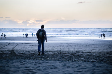 Man walking on Piha Beach. Unrecognizable people playing on the beach. Auckland.の写真素材