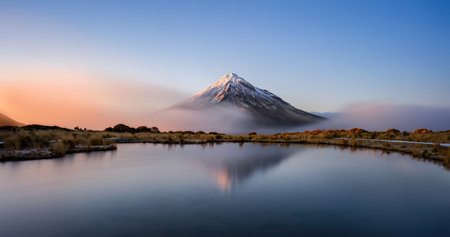 Snow-capped Mt Taranaki reflected in the clear water of Pouakai tarn at Sunrise, New Zealand.の写真素材