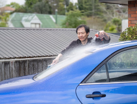 Man washing car windows using a brush and water spray from a hose.の写真素材
