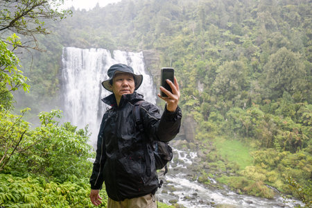 Tourist taking selfie photos using a smartphone in the rain. Marokopa Falls. Waikato. New Zealand.の写真素材