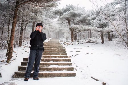 Young man taking photos using a small camera in the snow. Mount Huangshan. Anhui province. China.の写真素材