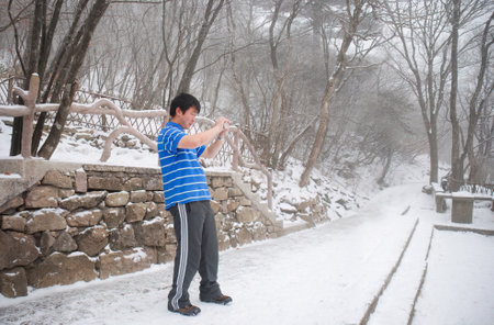 Young man taking photos in the snow. Anhui province. China.の写真素材
