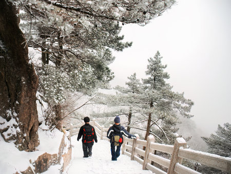 Two backpackers walking down the steps in the snow. Mount Huangshan. Anhui province. China.の写真素材