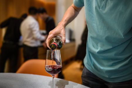 Man pouring red wine to the wine glasses at the restaurant. Unrecognizable staff in the background.