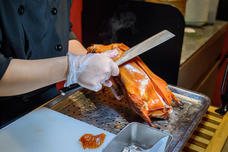 Hands of a chef holding a kitchen knife, carving roast Peking duck in a restaurant.の写真素材
