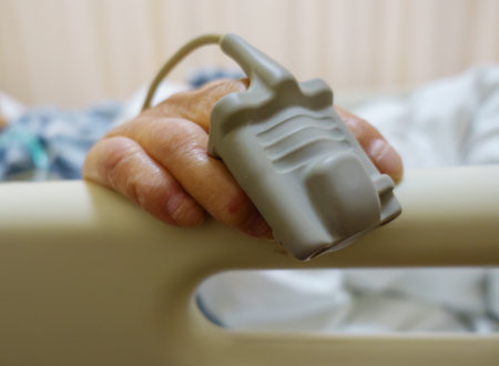 Hand of a senior woman wearing a pulse oximeter. Patient lying in hospital bed.の写真素材