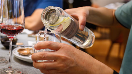 Hands of a man pouring water into a glass. Red wine glass on the side. Drinking water at the restaurant.の写真素材