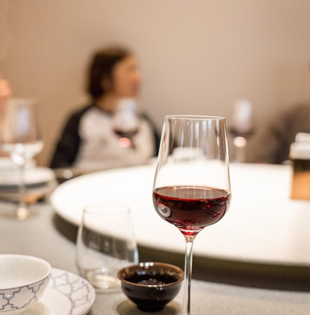 A glass of red wine on the restaurant table, an out-of-focus woman on the other side of the table.の写真素材