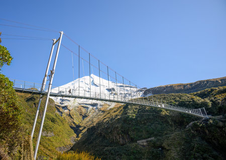 Tourist walking on Wanganui Gorge suspension bridge. Snow-capped Mt Taranaki in the background. Taranaki. New Zealand.の写真素材